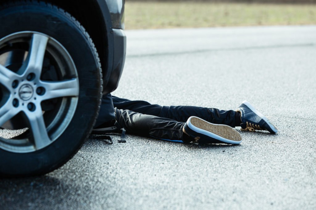 Ruedas de un coche cerca de las piernas de una víctima que acaba de ser atropellada en la carretera - causar un accidente con muerte o lesiones graves puede llevar a una audiencia de fatalidad del DMV