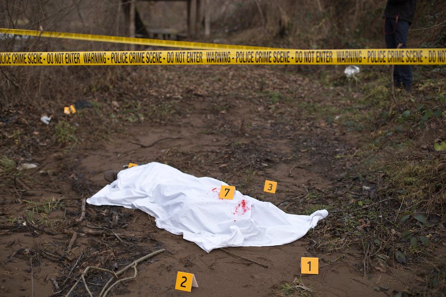 crime scene tape with sheet over body in ditch