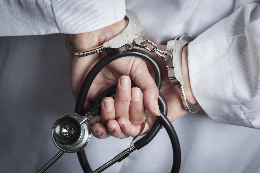 Closeup of doctors' hands holding stethascope in handcuffs after a Business and Professions Code 2052 violation