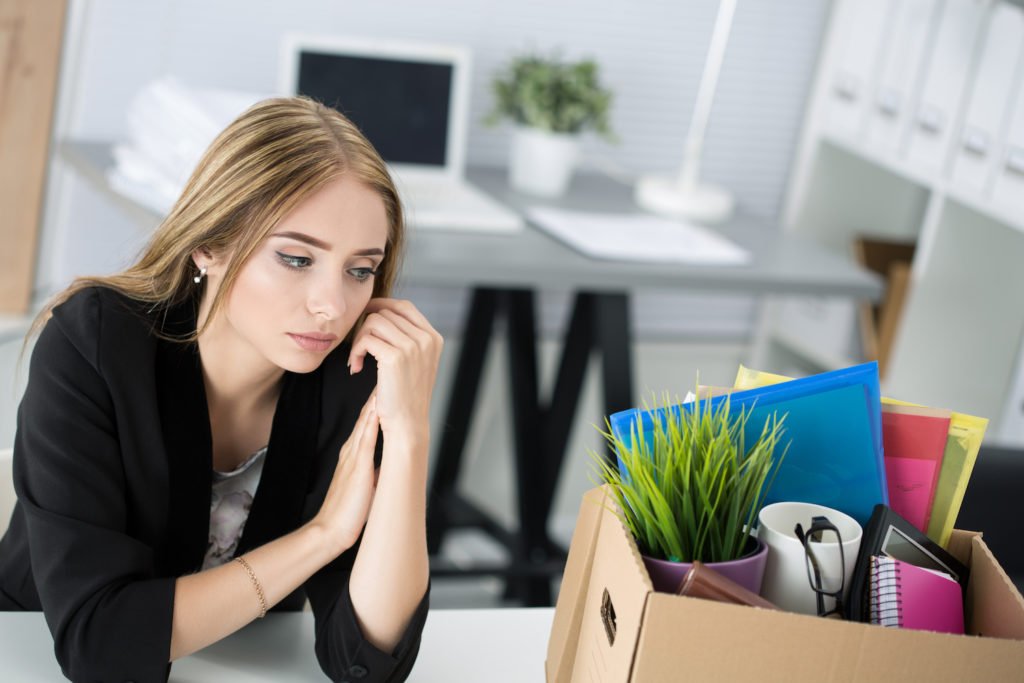 Fired employee next to box of belongings at old work desk