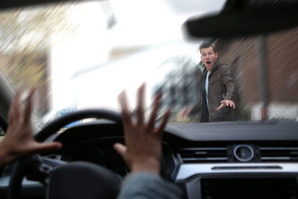 Driver about to hit a surprised looking pedestrian crossing the street