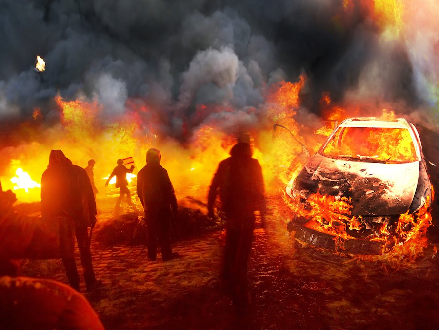 Cinco alborotadores cerca de un coche de policía que incendiaron como ejemplo de un delito de disturbios según el CRS 18-9-104 de Colorado