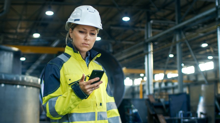 Trabajador con casco de seguridad sosteniendo un teléfono celular - muchos estados, incluida California, requieren reembolso por el uso de sus teléfonos celulares personales para fines comerciales