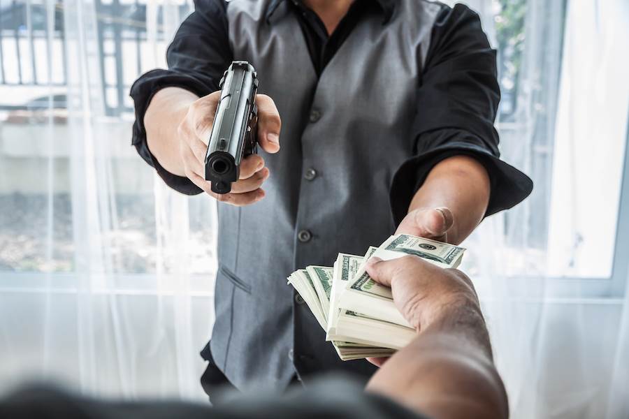 Hombre apuntando con un arma a una persona entregando dinero en un robo
