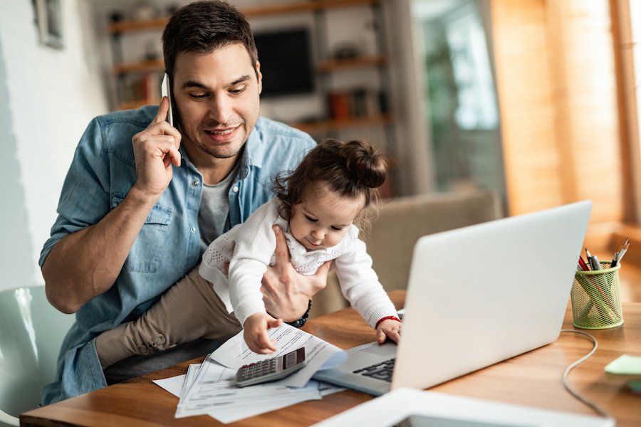 Dad with baby working from home in front of laptop - Labor Code 2802 requires certain home office expenses to be reimbursed