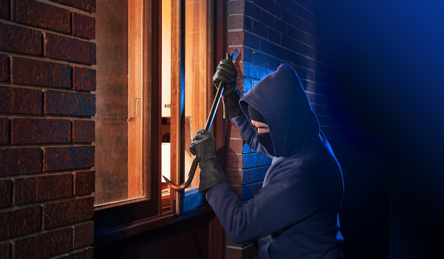 Hooded burglar with crowbar breaking into house window