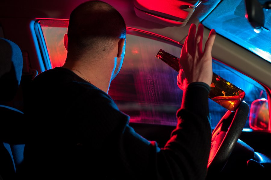 Conductor sosteniendo botella de cerveza viendo el coche de policía detrás de él