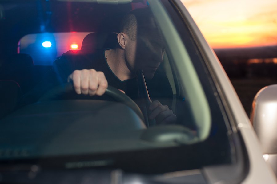 Conductor con botella de cerveza con luces de policía detrás de él