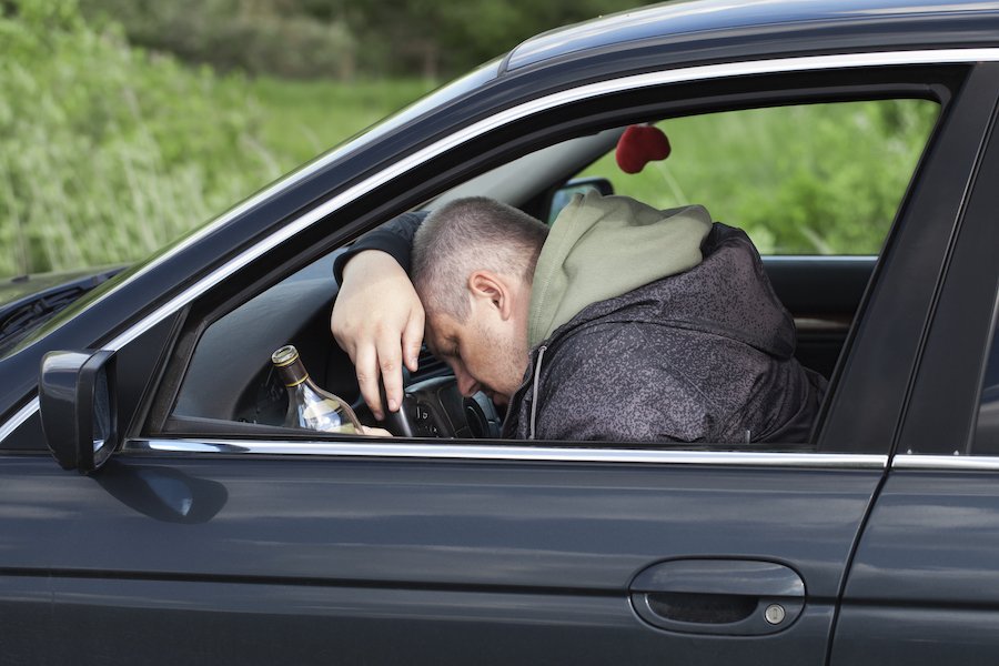 Hombre borracho inconsciente sobre el volante con botella de cerveza