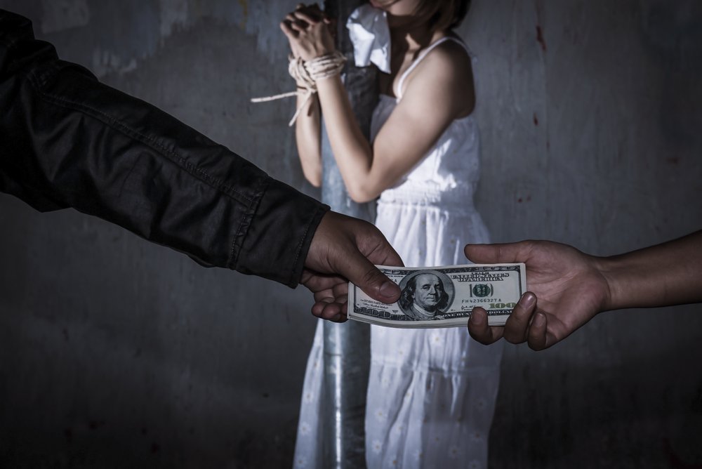 Mujer atada mientras se muestran dos manos intercambiando dinero.