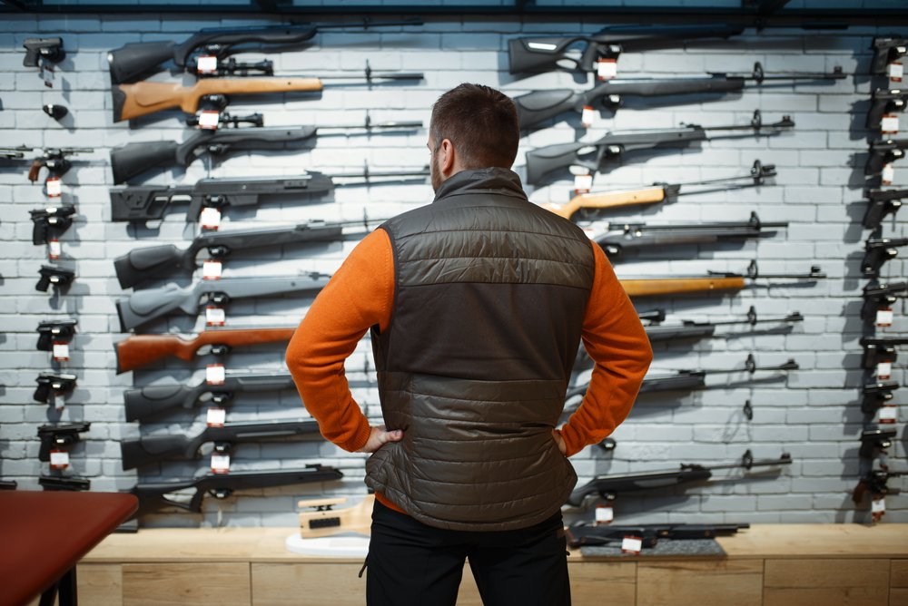 man looking at guns in a store - Penal Code 23515 PC imposes a firearm ban on people convicted of certain offenses