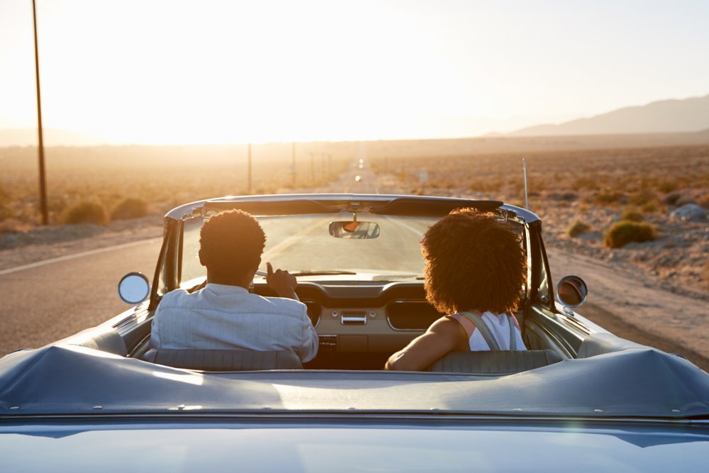 A couple driving a convertible towards the sunset.