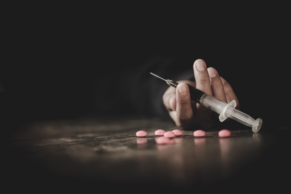 Hand holding a hypodermic needle, and some pills strewn next to it