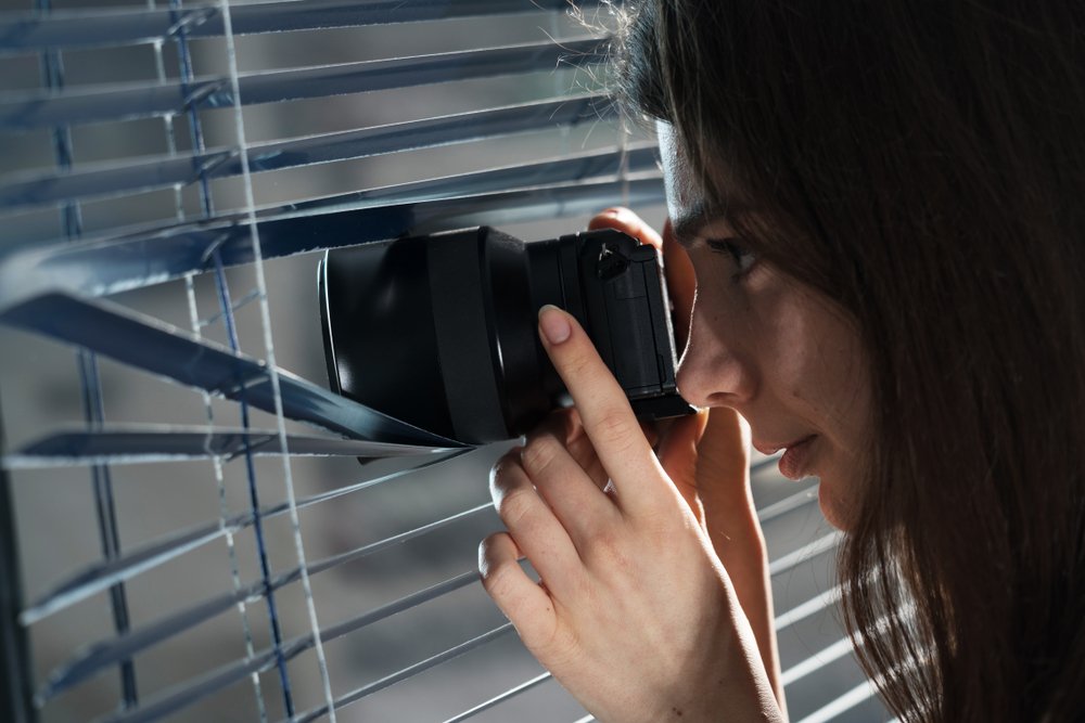 Mujer fotografiando secretamente a través de una rendija en las persianas.