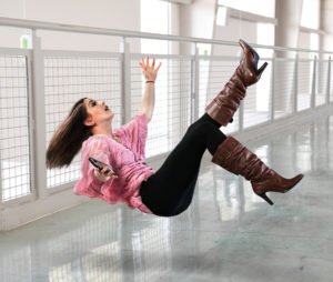 Young businesswoman falling on floor inside office building while holding phone