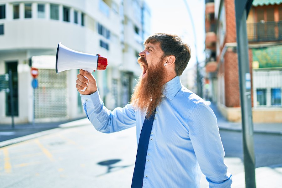 Young redhead businessman with angry expression screaming through a megaphone