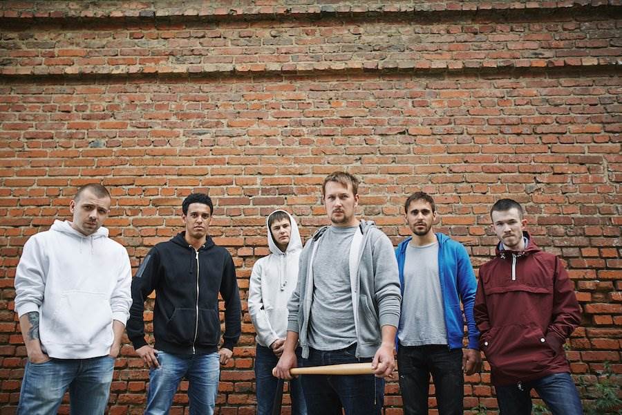 Gang of six in hoodies in front of brick wall