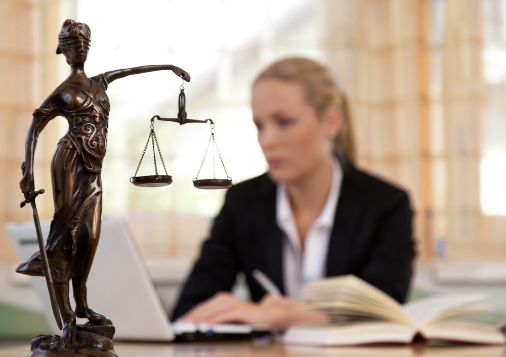 Abogado trabajando detrás de una estatua de una mujer ciega sosteniendo las escalas de la justicia