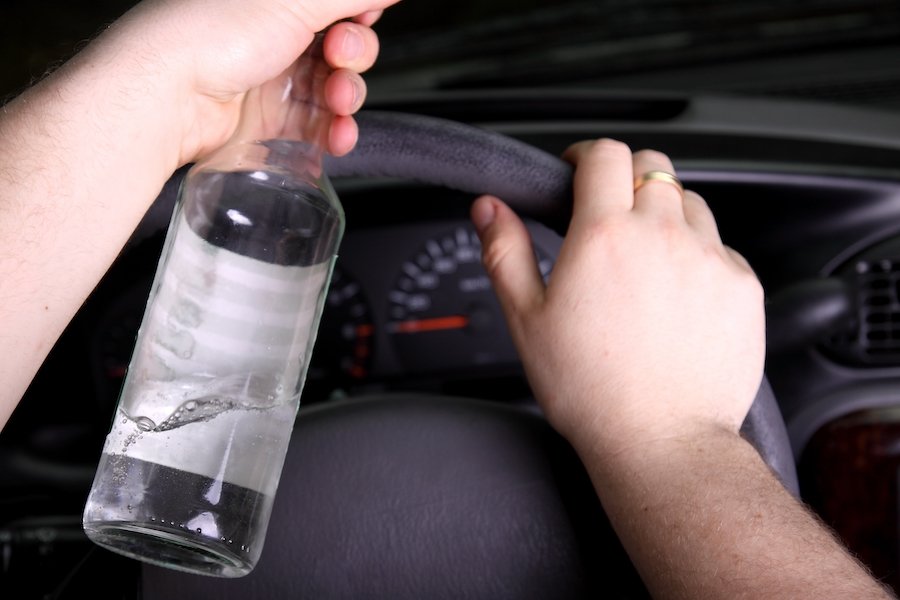 Driver with one hand on wheel and the other holding a beer