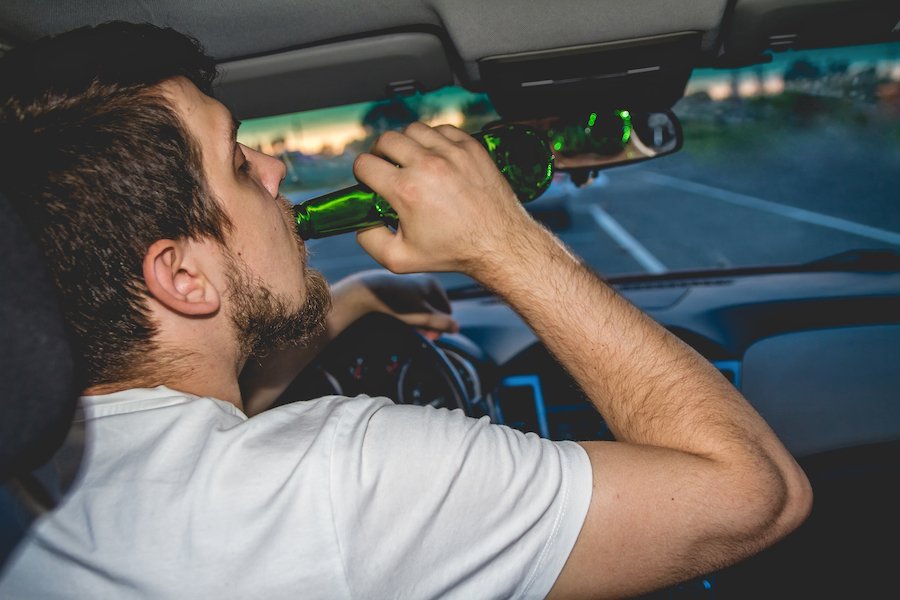 Conductor con una mano en el volante y la otra sosteniendo una cerveza