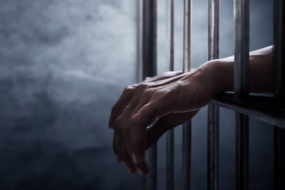 La mano de un recluso extendiéndose fuera de una celda de prisión: una violación del Código Penal 653b PC puede llevar a una detención de hasta 6 meses