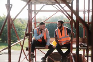 two construction workers eating while sitting on scaffolding 