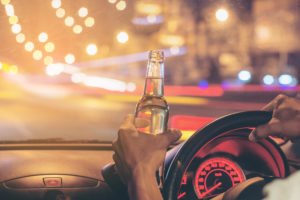 driver holding steering wheel with one hand and a beer in the other