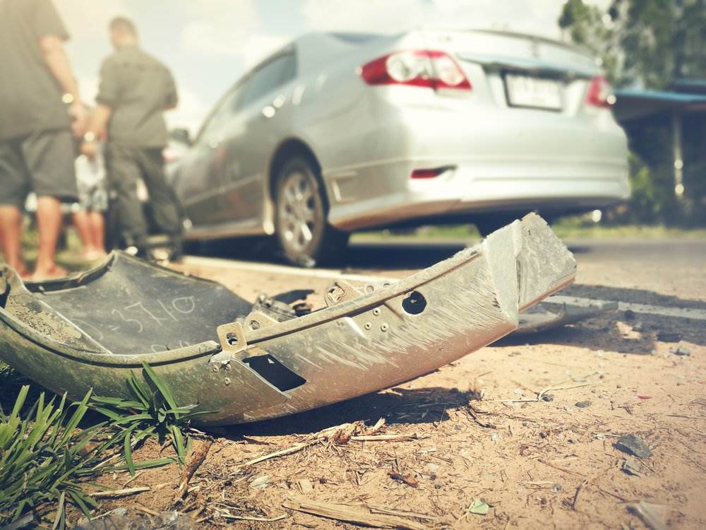 An accident scene with a fallen bumper on the side of the road.