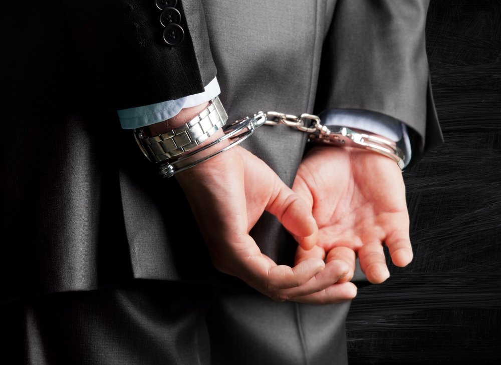 Suited man in handcuffs - a violation of Penal Code 186.10 PC is a felony punishable by up to 4 years in prison