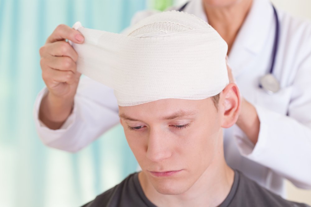 A young man having his head wrapped by a doctor after a traumatic injury.