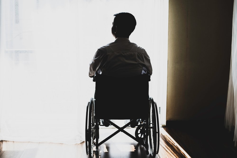 A wheelchair bound man staring out a window.