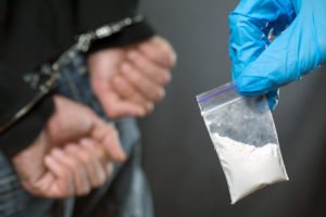 Imagen de una bolsa de cocaína y un traficante de drogas con esposas, quien enfrenta una sentencia aumentada bajo el Código de Salud y Seguridad de California 11370.4 HS