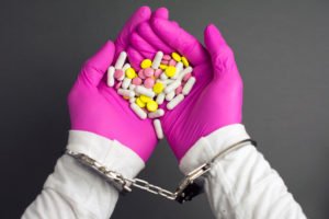 Gloved doctors hands in handcuffs holding illegally obtained prescription drugs in violation of NRS 453.421 