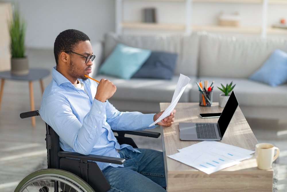 A wheelchair bound man reading a paper - California temporary disability rates for 2022 will remain at $203.44 per week