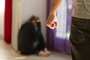 Man's fist with battered woman crouched in the background