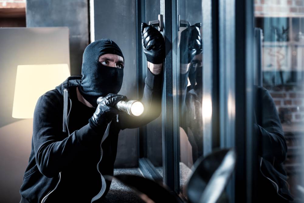 Hombre enmascarado con una linterna intentando entrar a una casa como ejemplo de delito agravado de allanamiento de morada