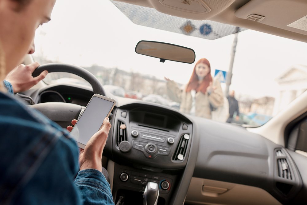 Un joven enviando mensajes de texto y conduciendo, a punto de atropellar a una joven mujer.