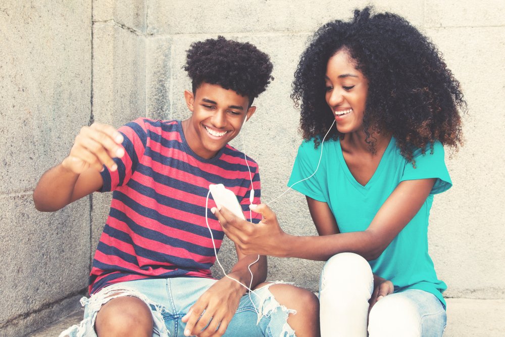 Two teens sharing headphones while listening to music on their smartphone.