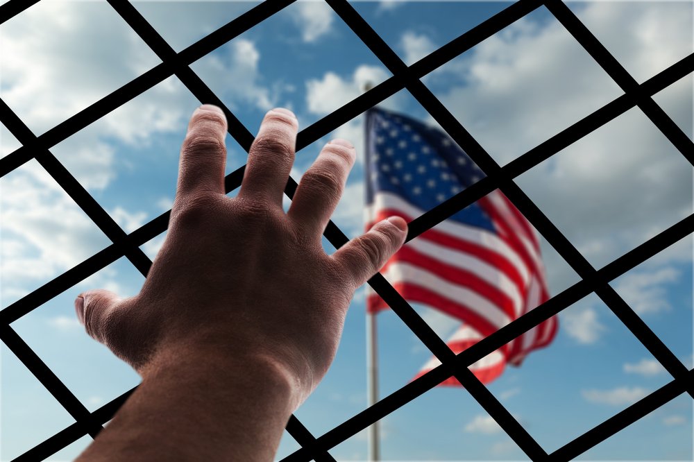 A hand holding onto a fence behind an American flag.
