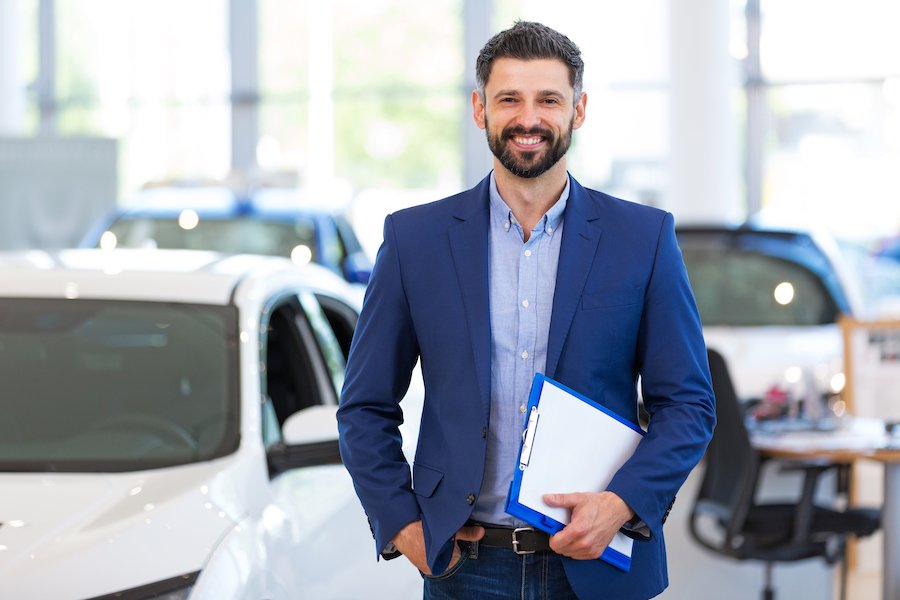 Vendedor de autos sonriente junto al inventario