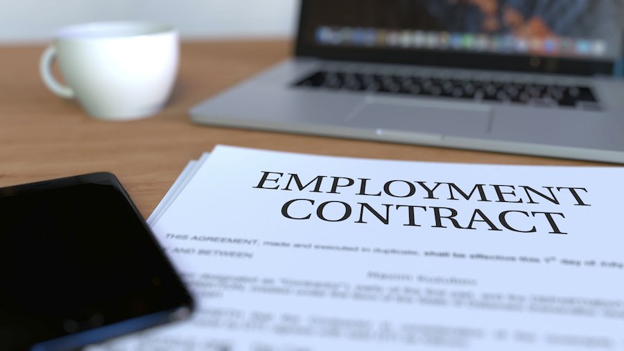 Paper that says "employment contract" on a desk next to a computer