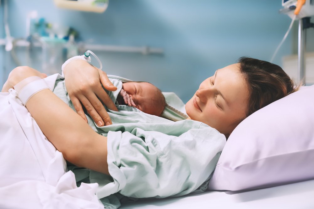 A mother with her new-born in a hospital bed, possibly on a leave of absence from work.