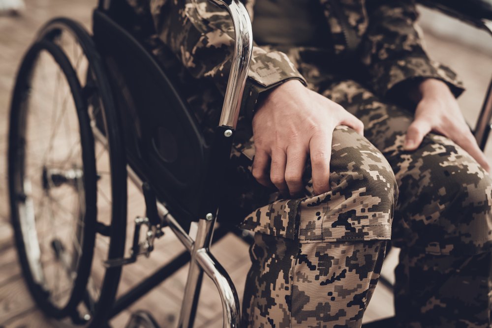 A man wearing military fatigues sits injured in a wheelchair.