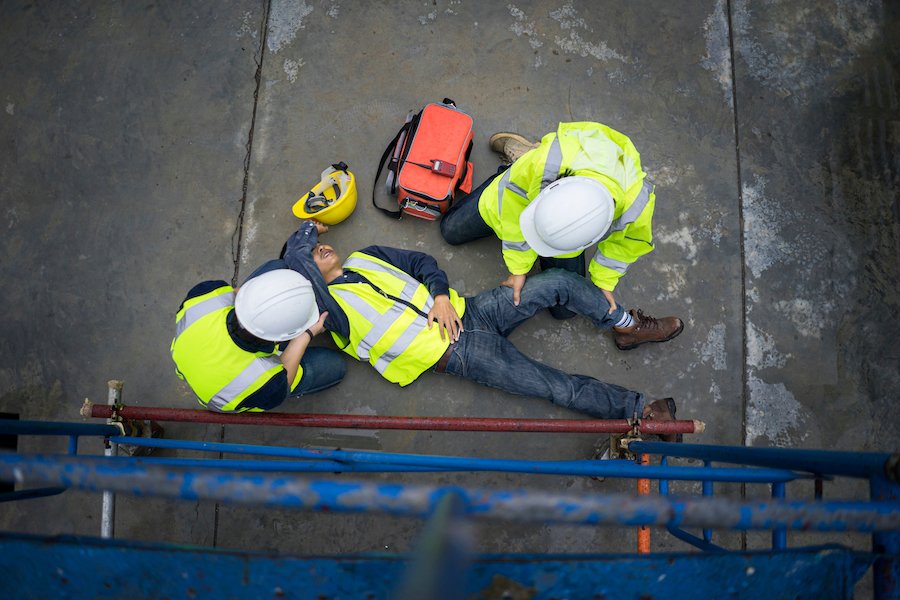 Secuelas de un accidente de construcción con trabajadores con cascos ayudando a la víctima en el suelo