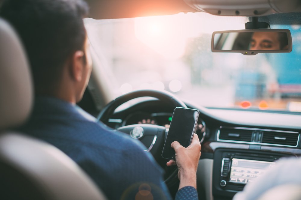 A distracted rideshare driver looking down at his smartphone while driving.