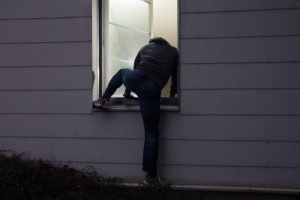 Burglar climbing into a house through a window