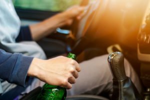 Man driving with one hand on steering wheel and the other holding a beer bottle