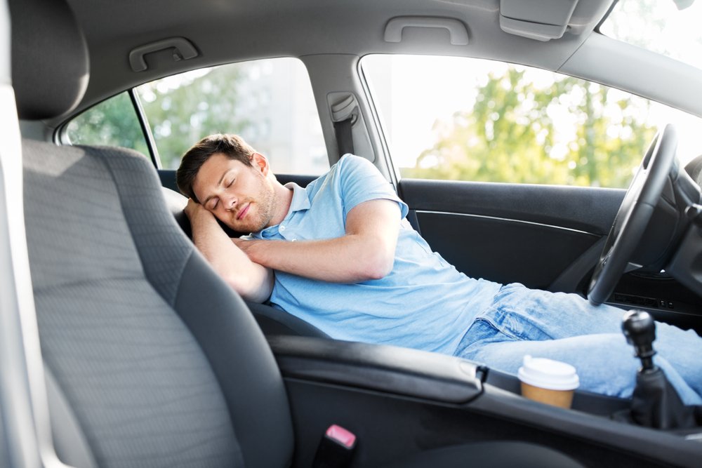 A man napping in his car, trying to sober up to avoid driving drunk.