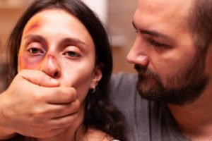 Woman with black eye with her abusing husband holding her mouth