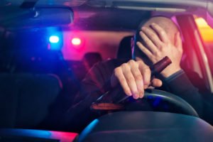 Driving holding a beer with police lights behind him